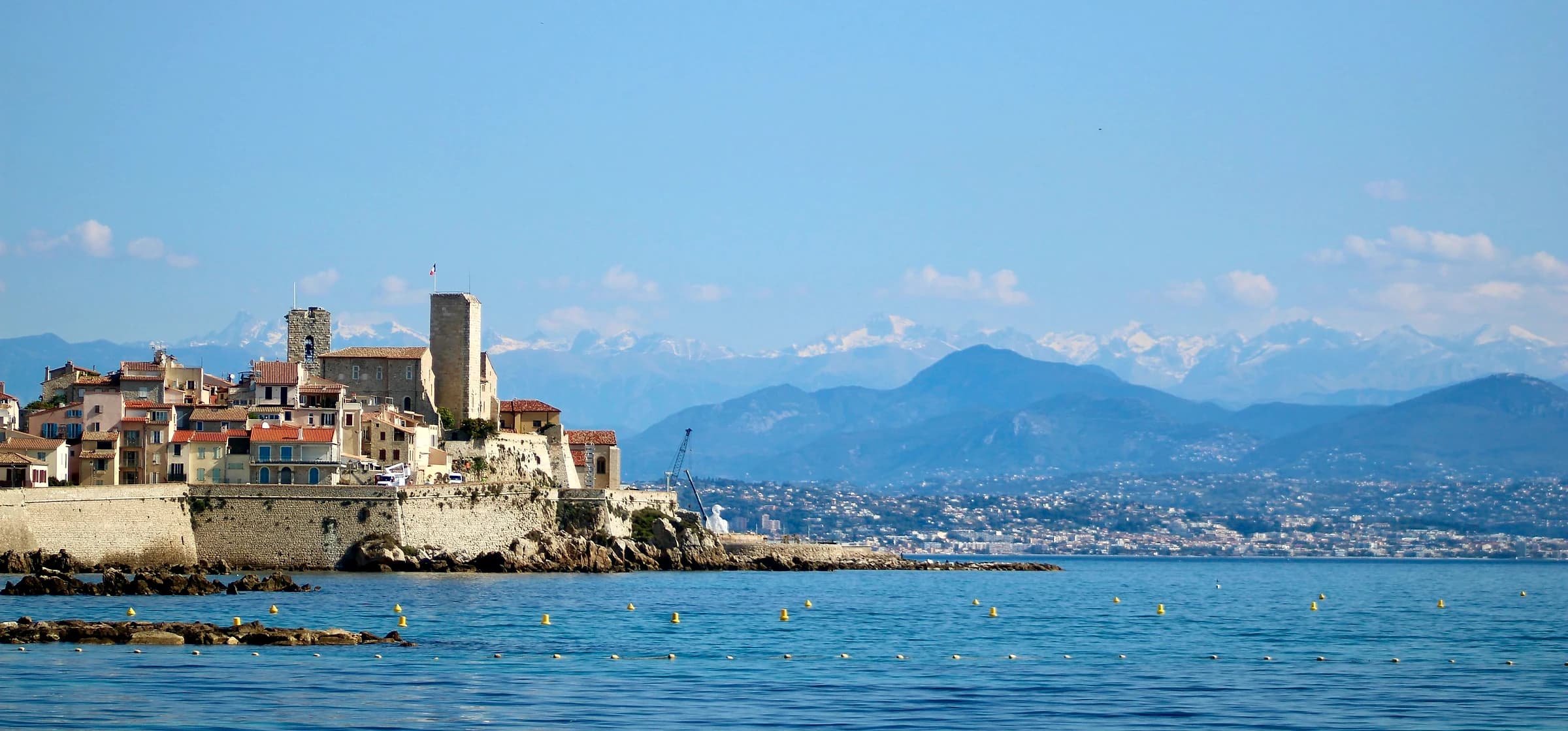 Les remparts et la vieille ville d'Antibes vus depuis la mer, avec les Alpes enneigées en arrière-plan